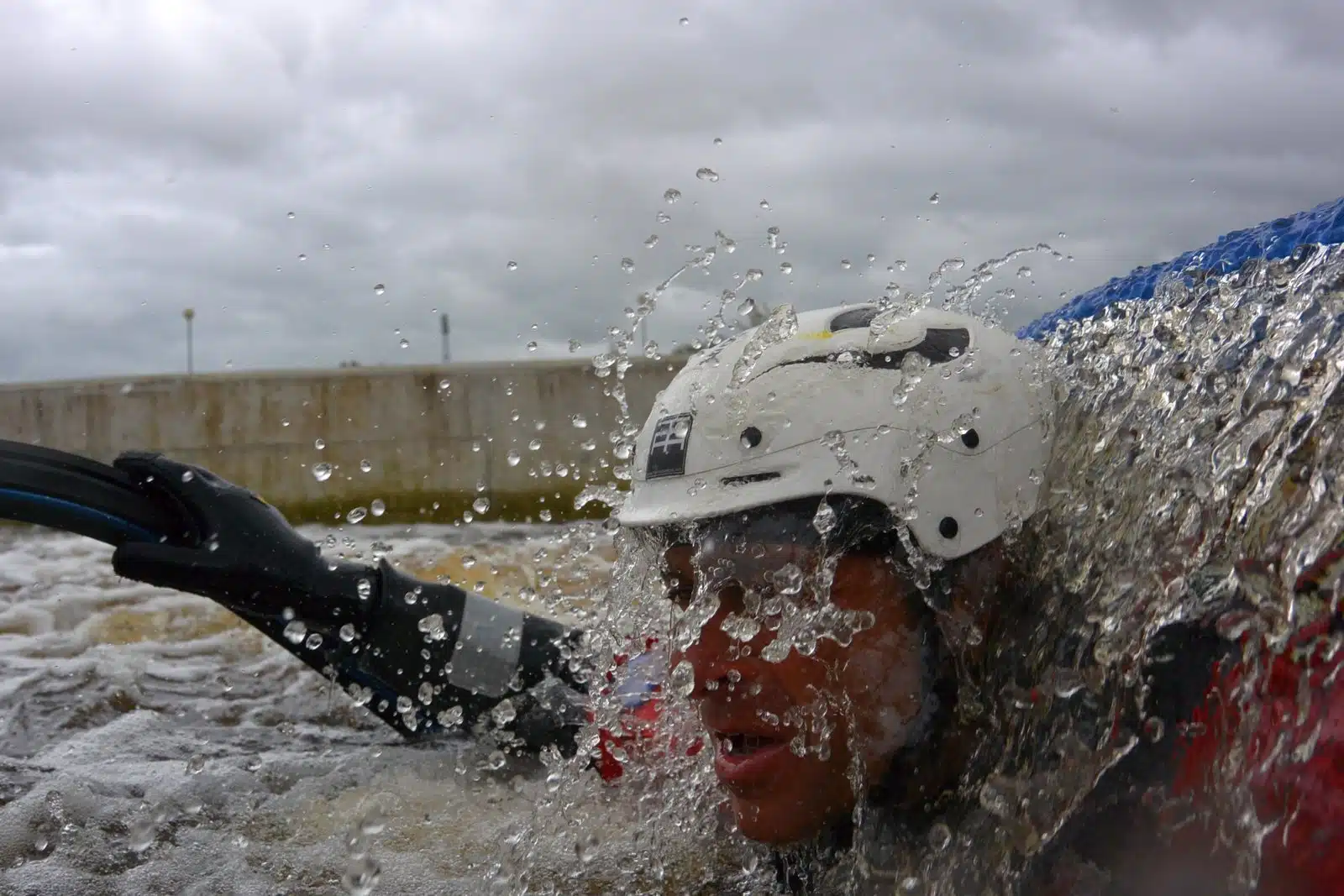 Soccorso Alluvionale e Fluviale Europa Un uomo con casco e muta, molto simile all'avventuriero David Alemanni, viene travolto da acque agitate mentre il cielo nuvoloso incombe sulla sua testa. S.A.F.E.® - River Rescue