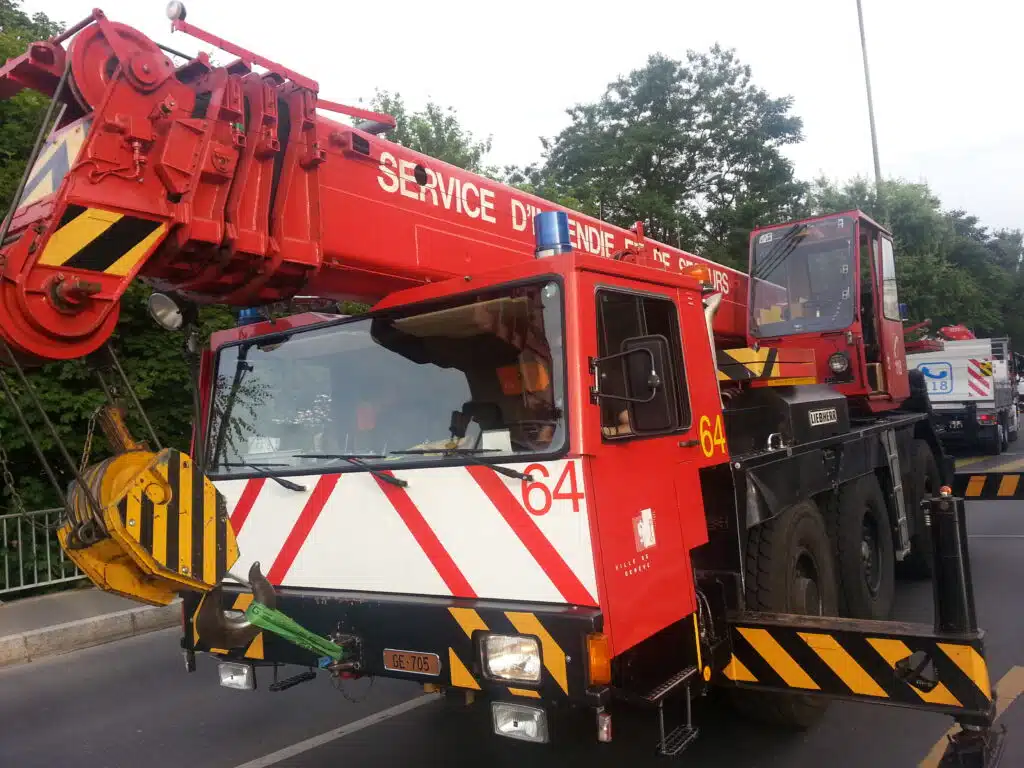Soccorso Alluvionale e Fluviale Europa Un'autogru rossa dei vigili del fuoco è ferma sulla strada, circondata da alberi e con un altro veicolo sullo sfondo, pronta per le operazioni di Rescue 3. S.A.F.E.® - River Rescue