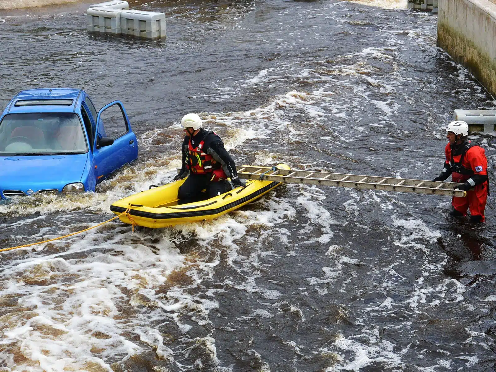 Soccorso Alluvionale e Fluviale Europa La squadra di soccorso 3 manovra con perizia una barca e una scala per soccorrere un'auto blu parzialmente sommersa durante l'alluvione. S.A.F.E.&reg; - River Rescue