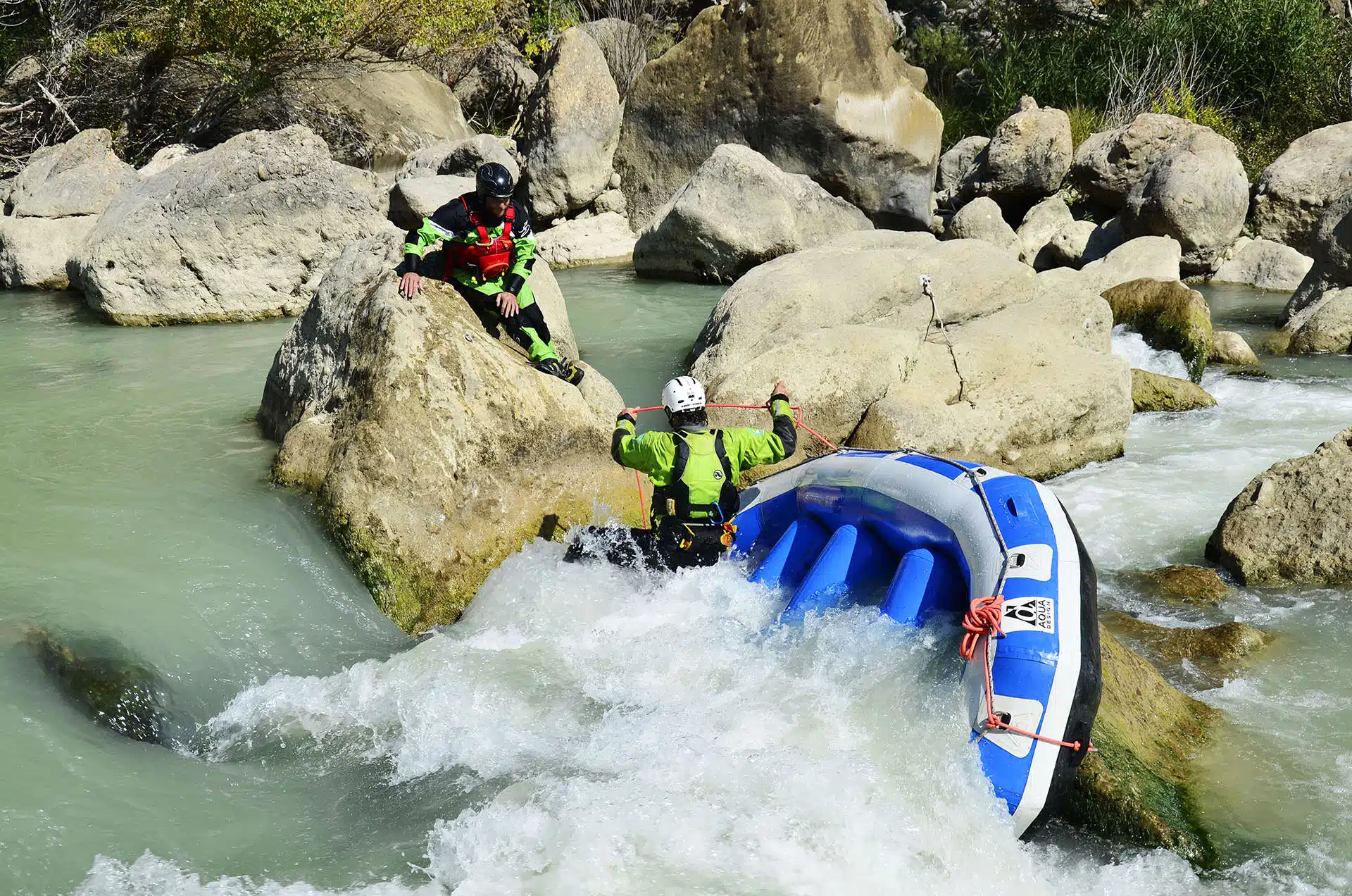 Soccorso Alluvionale e Fluviale Europa Due persone in equipaggiamento di sicurezza, simili a kayakisti esperti, guidano un gommone tra rapide rocciose. Uno sta in piedi con sicurezza su una roccia, fungendo da guida per l'altro nel gommone WRT Pro. S.A.F.E.® - River Rescue
