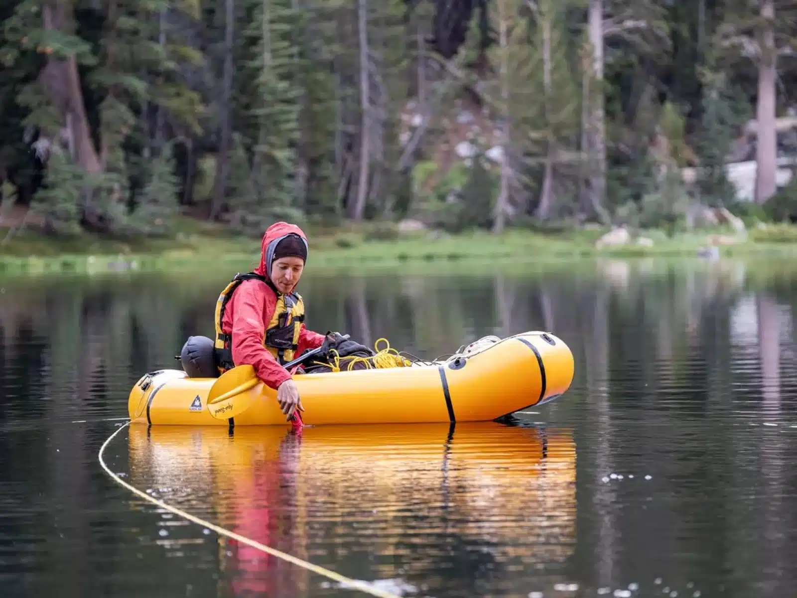 Soccorso Alluvionale e Fluviale Europa Un uomo con una giacca rossa e un berretto guida una zattera gialla su un lago boscoso, tirando abilmente una corda dall'acqua, incarnando lo spirito di Rescue 3. S.A.F.E.&reg; - River Rescue