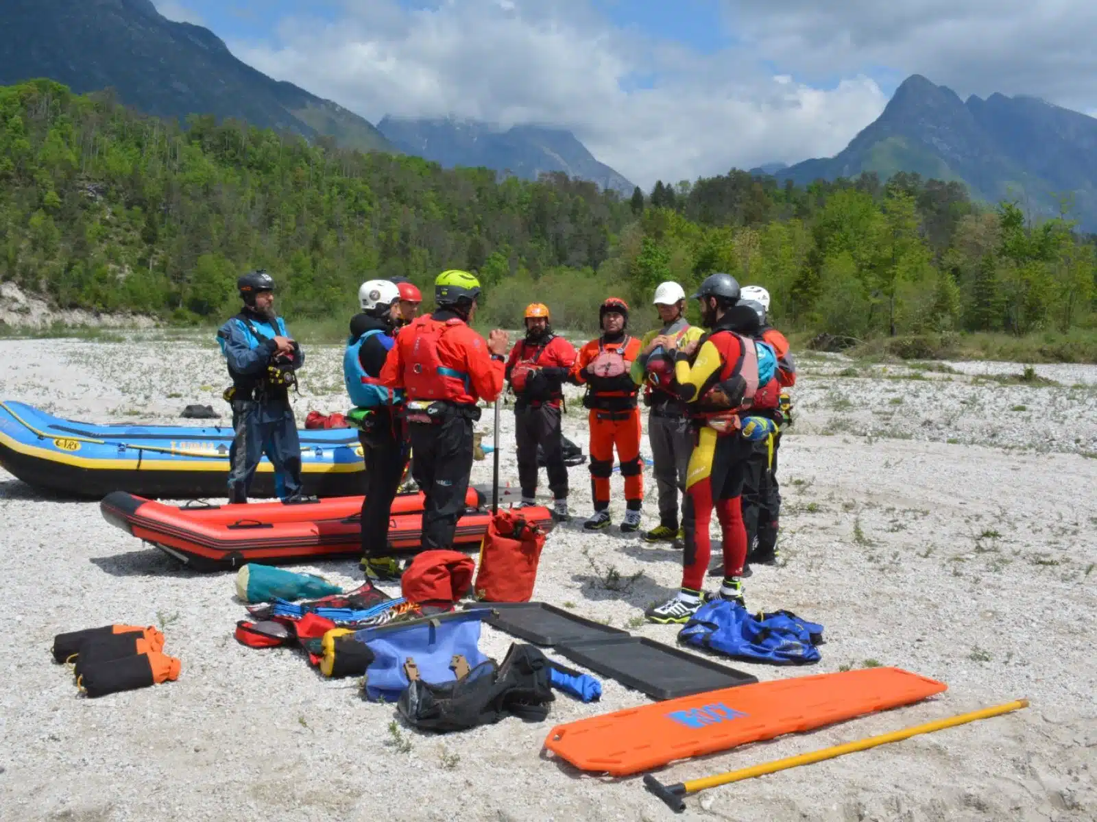 Soccorso Alluvionale e Fluviale Europa Un gruppo di persone in equipaggiamento colorato, forse membri del Rescue 3, si raduna attorno all'attrezzatura accanto alle zattere, con maestose montagne che si ergono fiere sullo sfondo. S.A.F.E.&reg; - River Rescue
