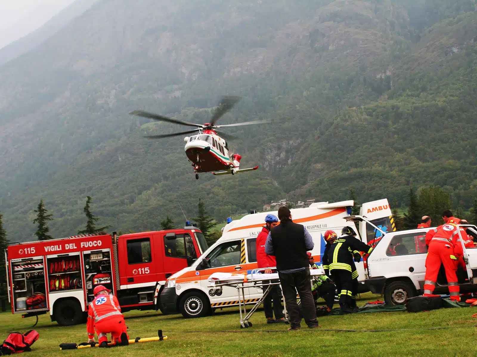 Soccorso Alluvionale e Fluviale Europa I soccorritori del team Rescue 3 intervengono sulla scena dell'incidente, mentre un elicottero atterra, circondato da veicoli e montagne maestose. S.A.F.E.&reg; - River Rescue