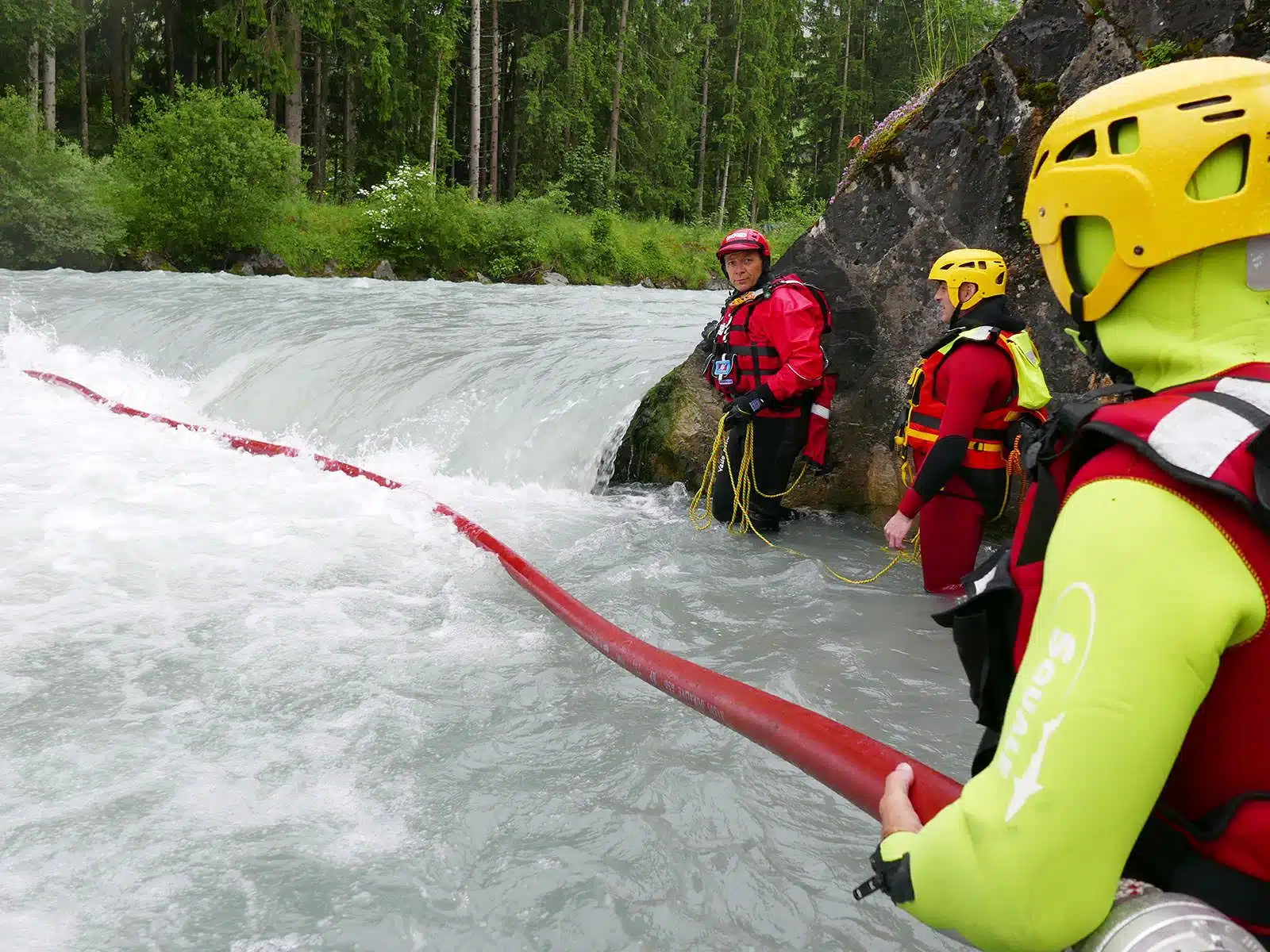 Soccorso Alluvionale e Fluviale Europa I membri della squadra di soccorso 3, dotati di caschi e mute, manovrano abilmente con una pompa vicino alla riva di un fiume, in una rigogliosa area boschiva. S.A.F.E.&reg; - River Rescue