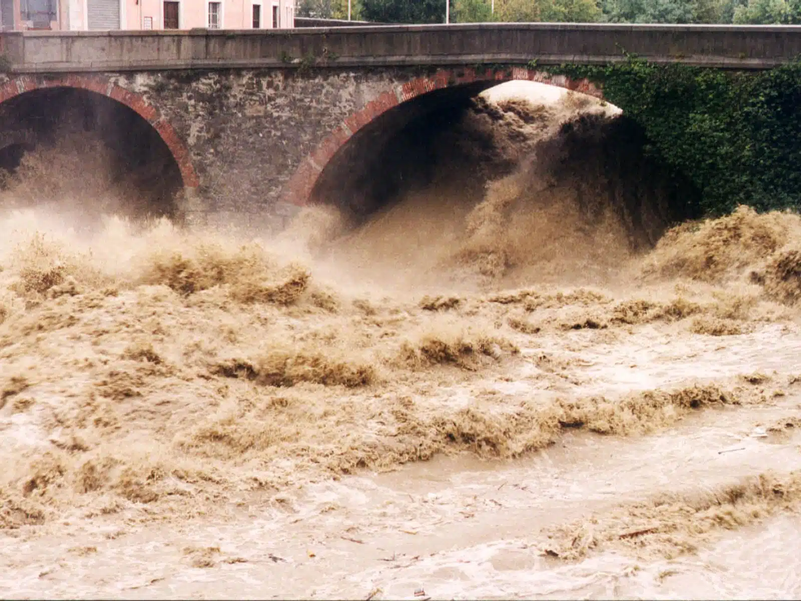 Soccorso Alluvionale e Fluviale Europa Le acque alluvionali si riversano sotto un ponte di pietra con aperture ad arco, creando potenti onde fangose che mettono a dura prova gli sforzi di soccorso. S.A.F.E.&reg; - River Rescue